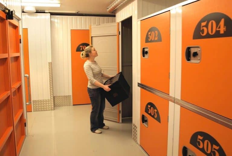 Asiakas kantaa tavaroita käytävällä. Oransseissa ovissa on isot numerokyltit.