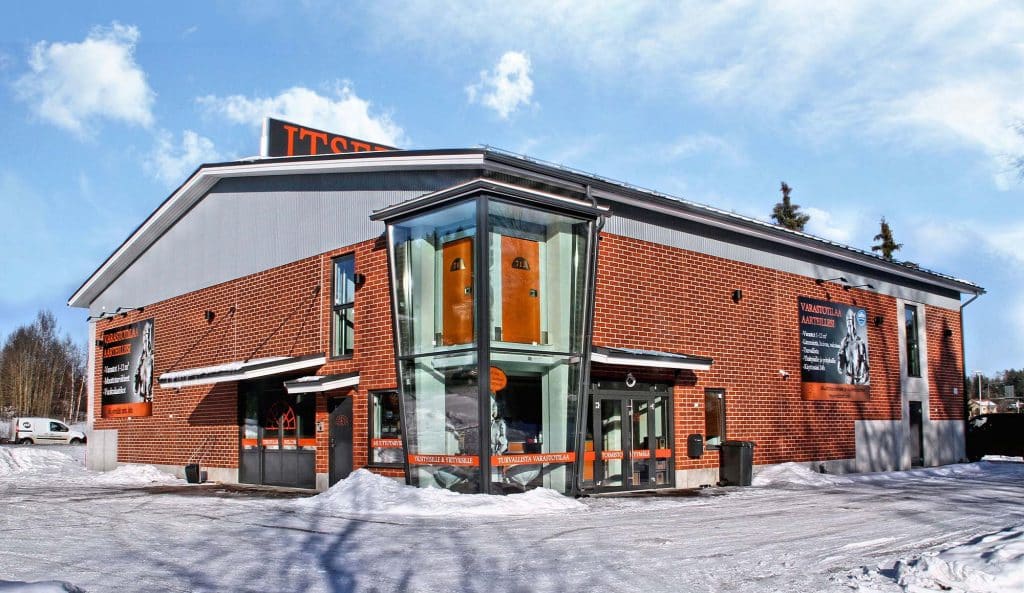 Holvin punatiilinen varastorakennus talvella. Sisäänkäynnin kohdalla on lasinen porrashuone ja oransseja paneeleja.